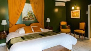A hotel room with a large bed, two chairs, a nightstand, a lamp, and a painting on the wall. - Hôtel de la Cognette (Issoudun)