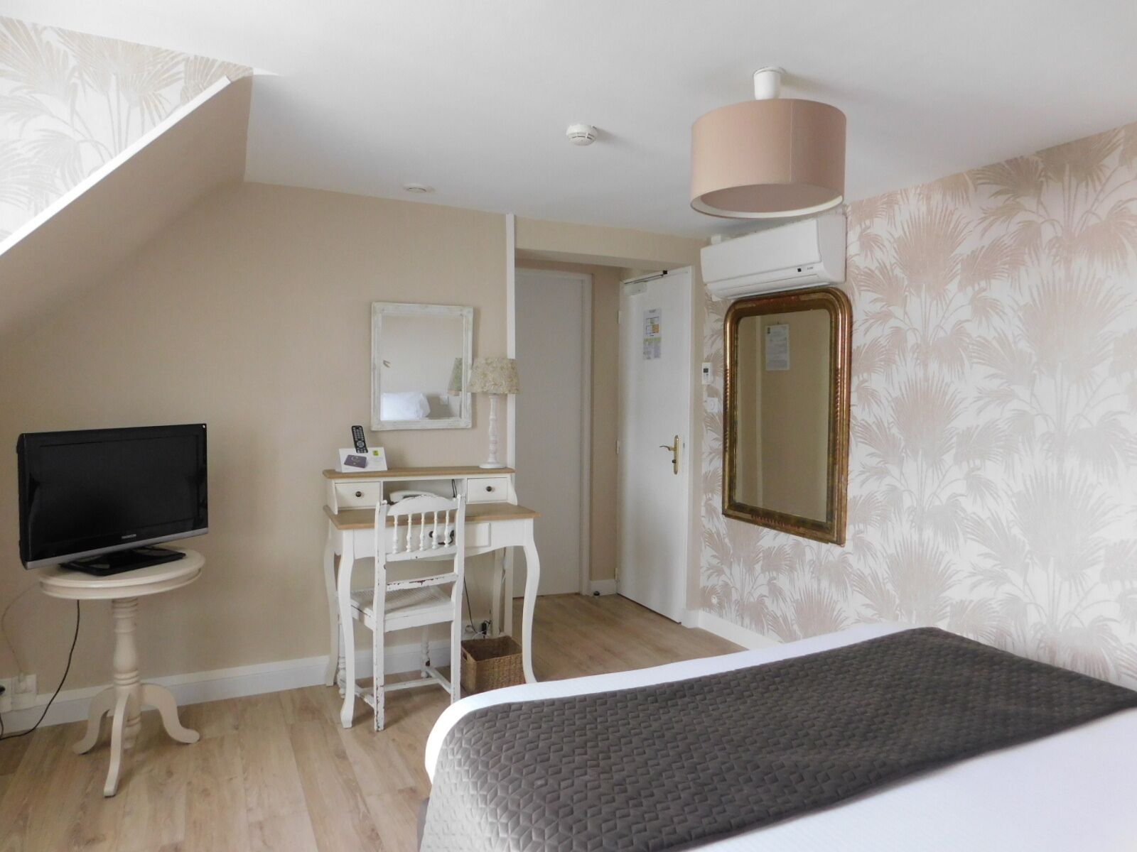 A bedroom with a bed, a desk with a chair, a television, and a door.