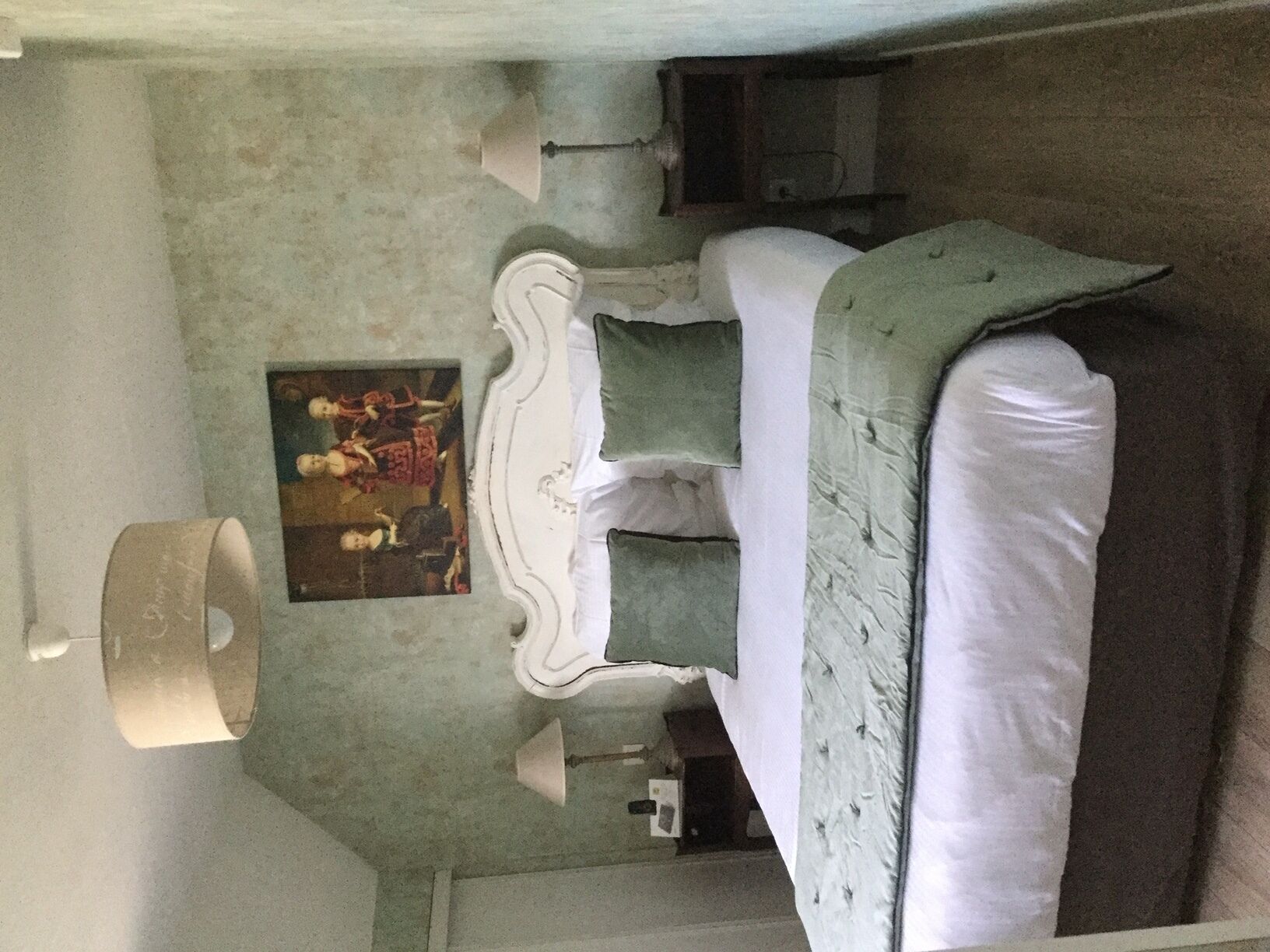 A bedroom with a bed, a nightstand, a lamp, and a painting on the wall.