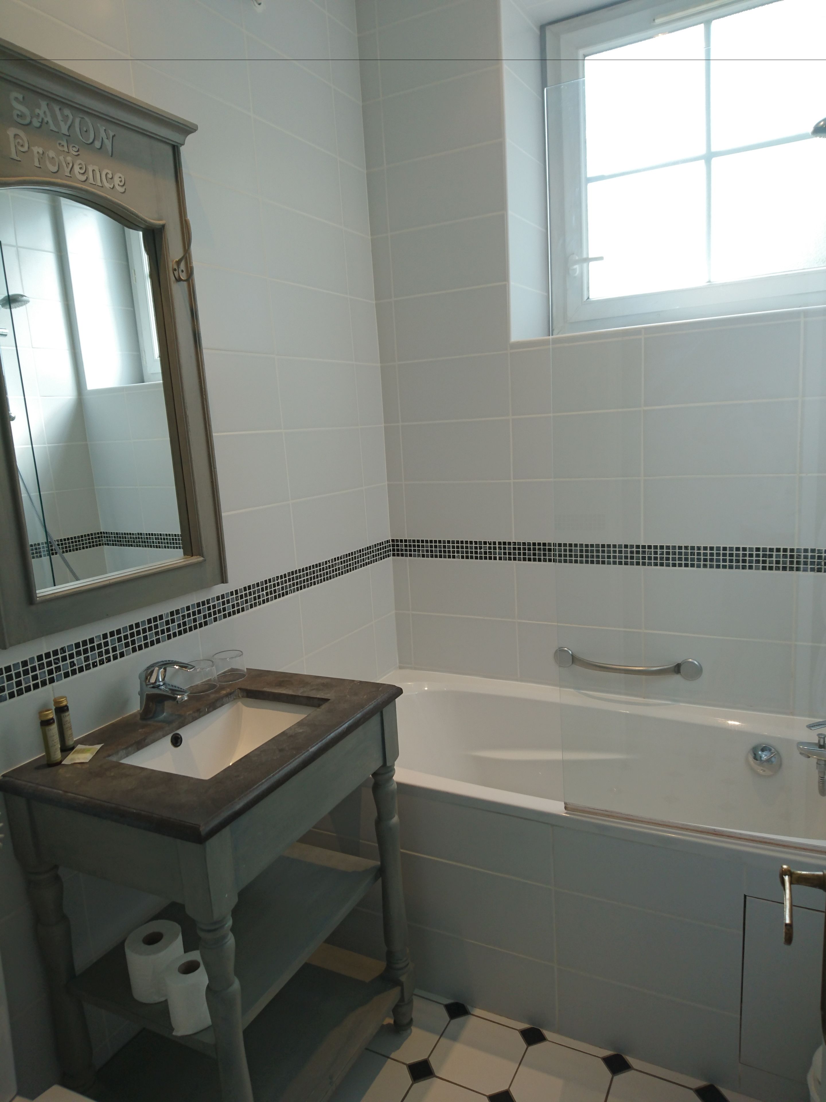 A bathroom with a white sink, a mirror, a bathtub, and a window.