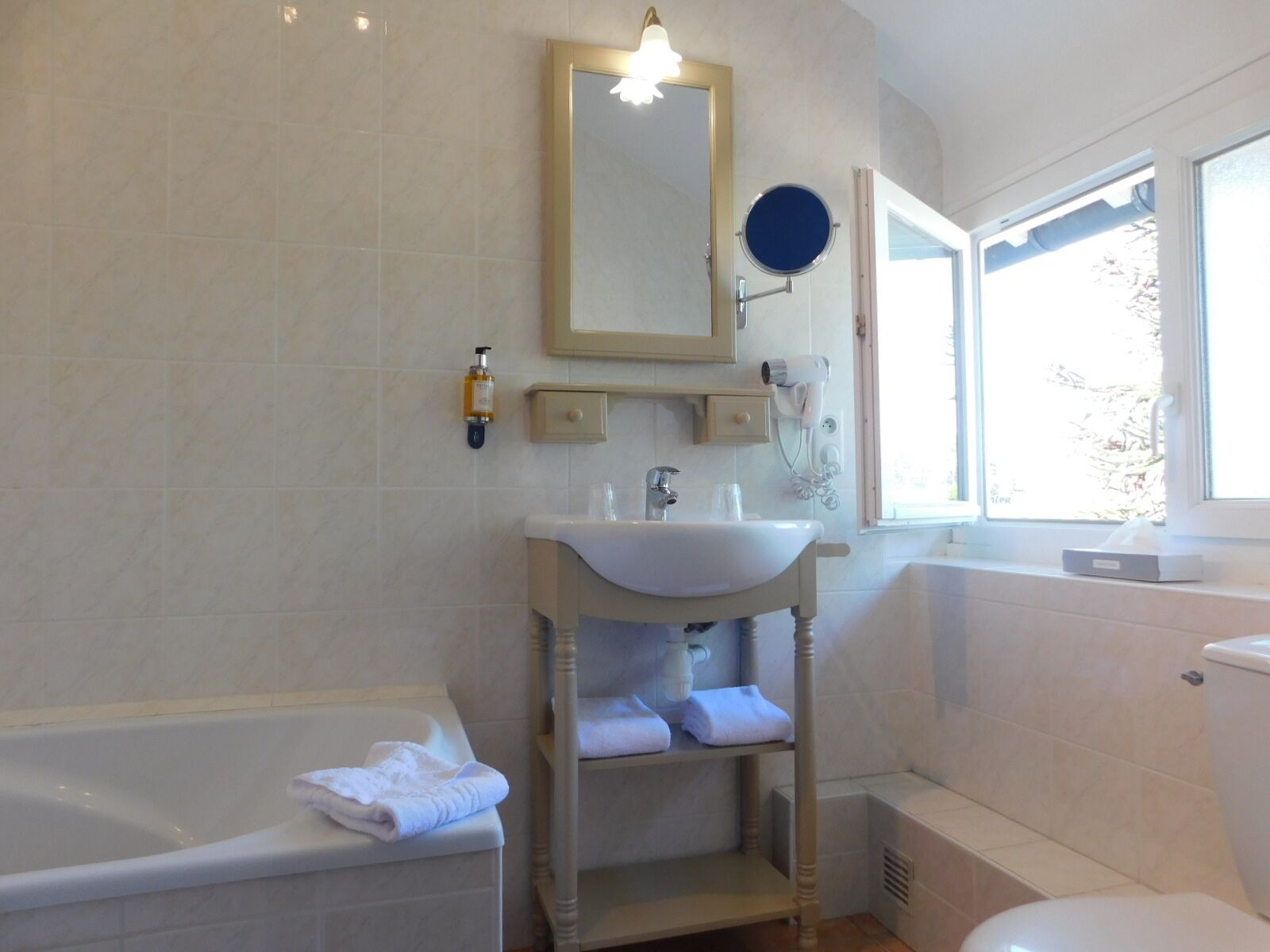 A bathroom with a bathtub, a sink, a mirror, a hairdryer, and a window.