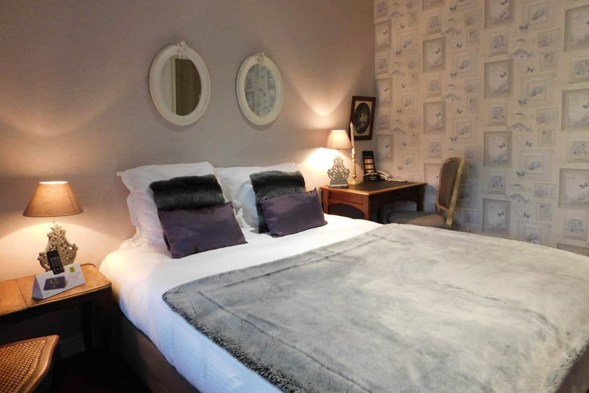 Una habitación de hotel con una cama, dos mesitas de noche, una silla y una pared decorada con cuadros.