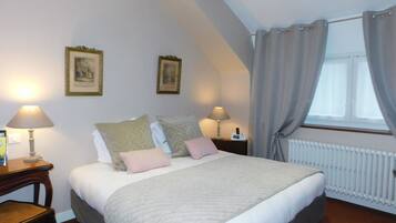 A bedroom with a large bed, two bedside tables with lamps, a radiator, and two framed pictures on the wall.