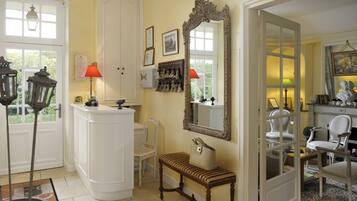 A room with a white door, a bench, a mirror, and a table with a lamp.