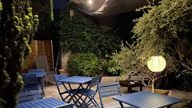 An outdoor patio area with blue metal tables and chairs, string lights, and a lantern. - Hôtel Colbert Tours (Tours)