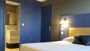 A hotel room with a large bed, a wardrobe, a bathroom with a mirror, and a wall-mounted light fixture. - Hôtel Colbert Tours (Tours)