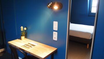 Une pièce avec un bureau en bois, une chaise, une lampe fixée au mur et un lit superposé.