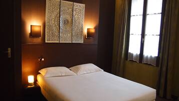 Ein Hotelzimmer mit einem Bett, zwei Wandleuchten, einer Wanddekoration und einem mit Vorhängen versehenen Fenster.