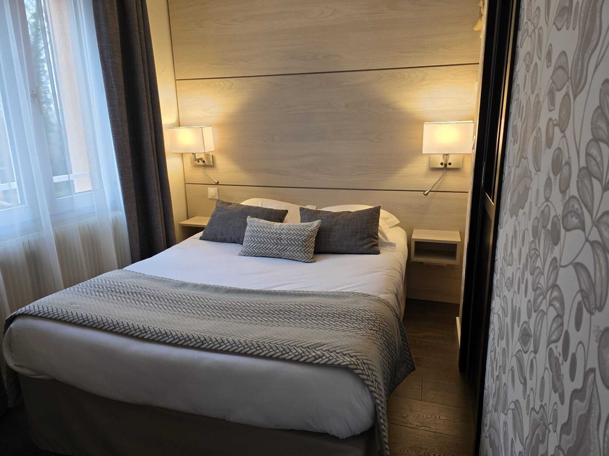 A neatly made bed with a patterned bedspread and pillows, two bedside lamps, and a wooden headboard.