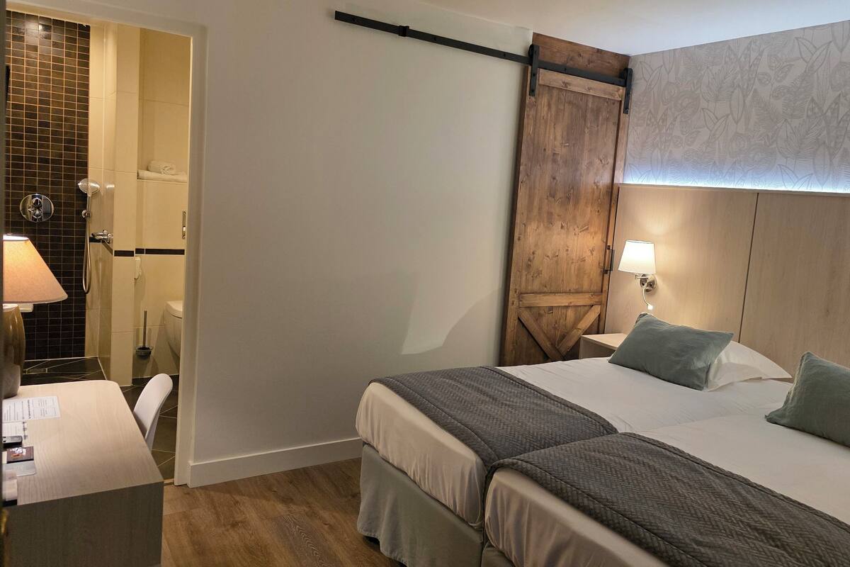 A hotel room with a bed, bedside tables, a desk, and a shower area.