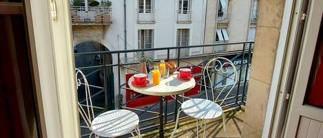 A balcony with a table and chairs, a red carpet, and a view of buildings in the background.
