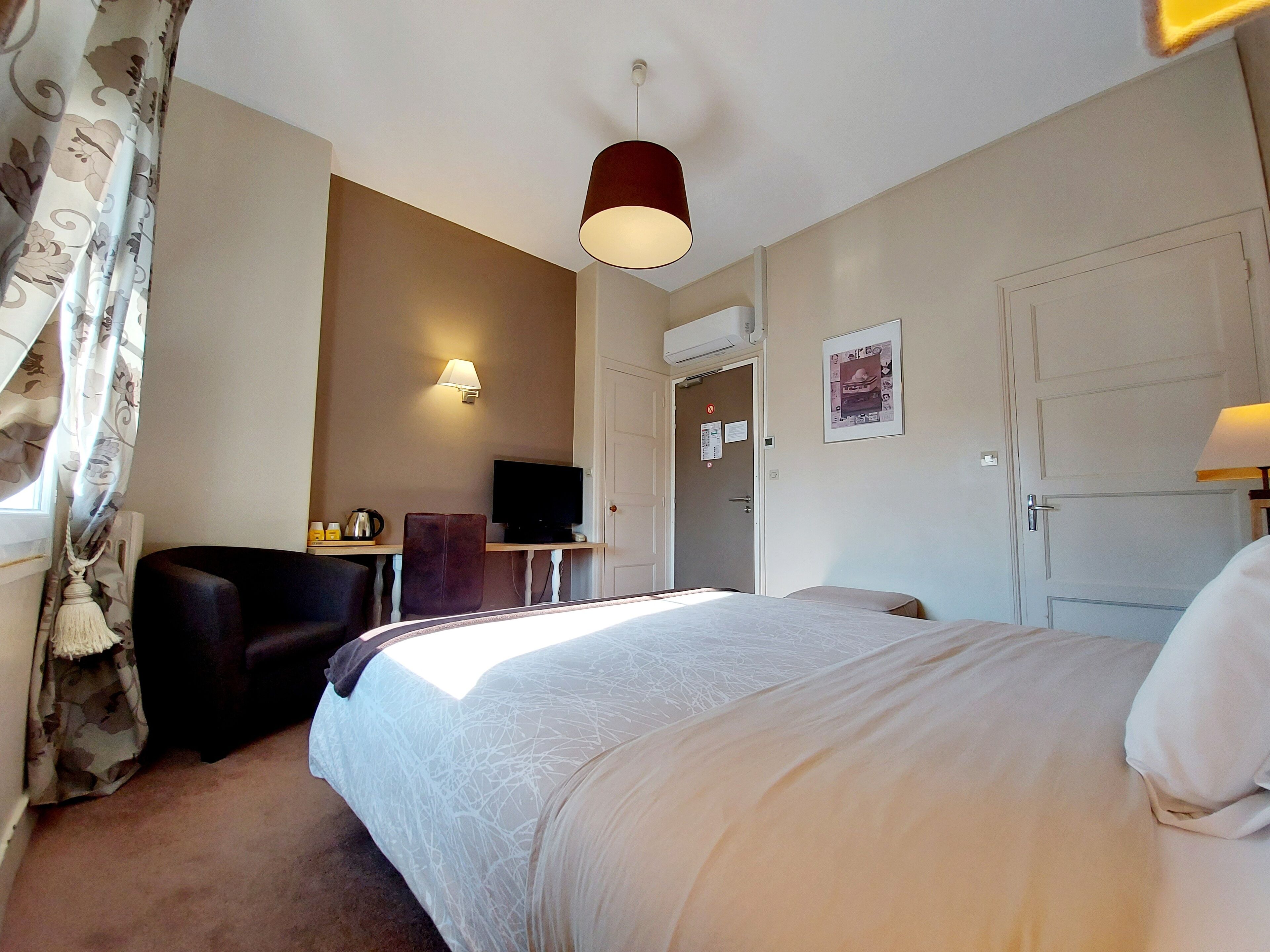 A hotel room with a bed, a desk with a computer, a chair, a television, and a door.