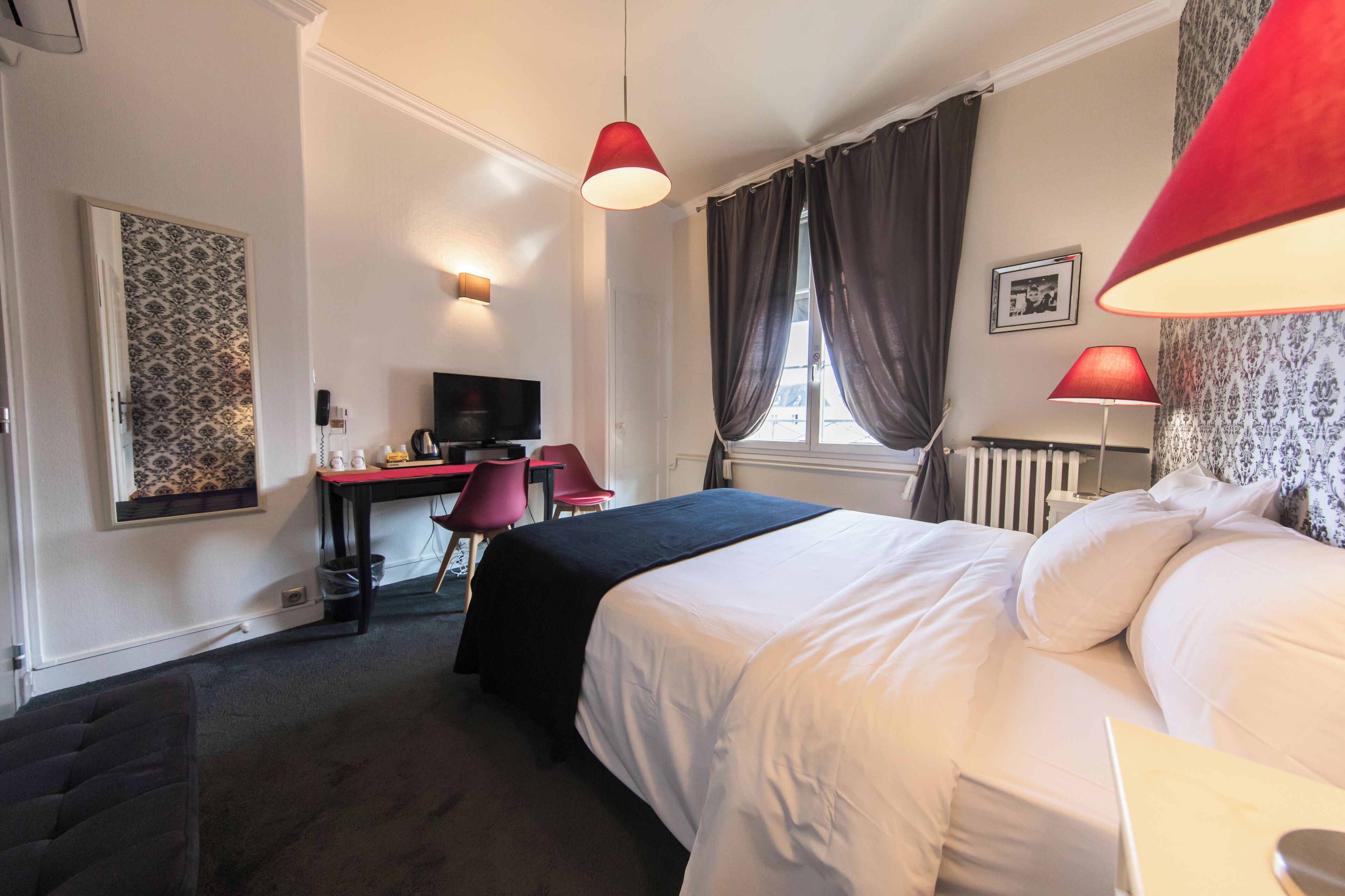 A hotel room with a bed, desk, chair, and two red lamps.