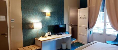A hotel room with a desk, television, and two beds.