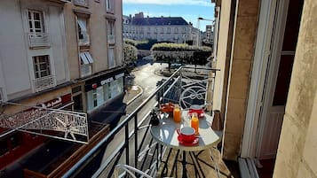 Un balcon avec une table dressée pour le petit-déjeuner, donnant sur une rue bordée d’immeubles et traversée par une rivière.