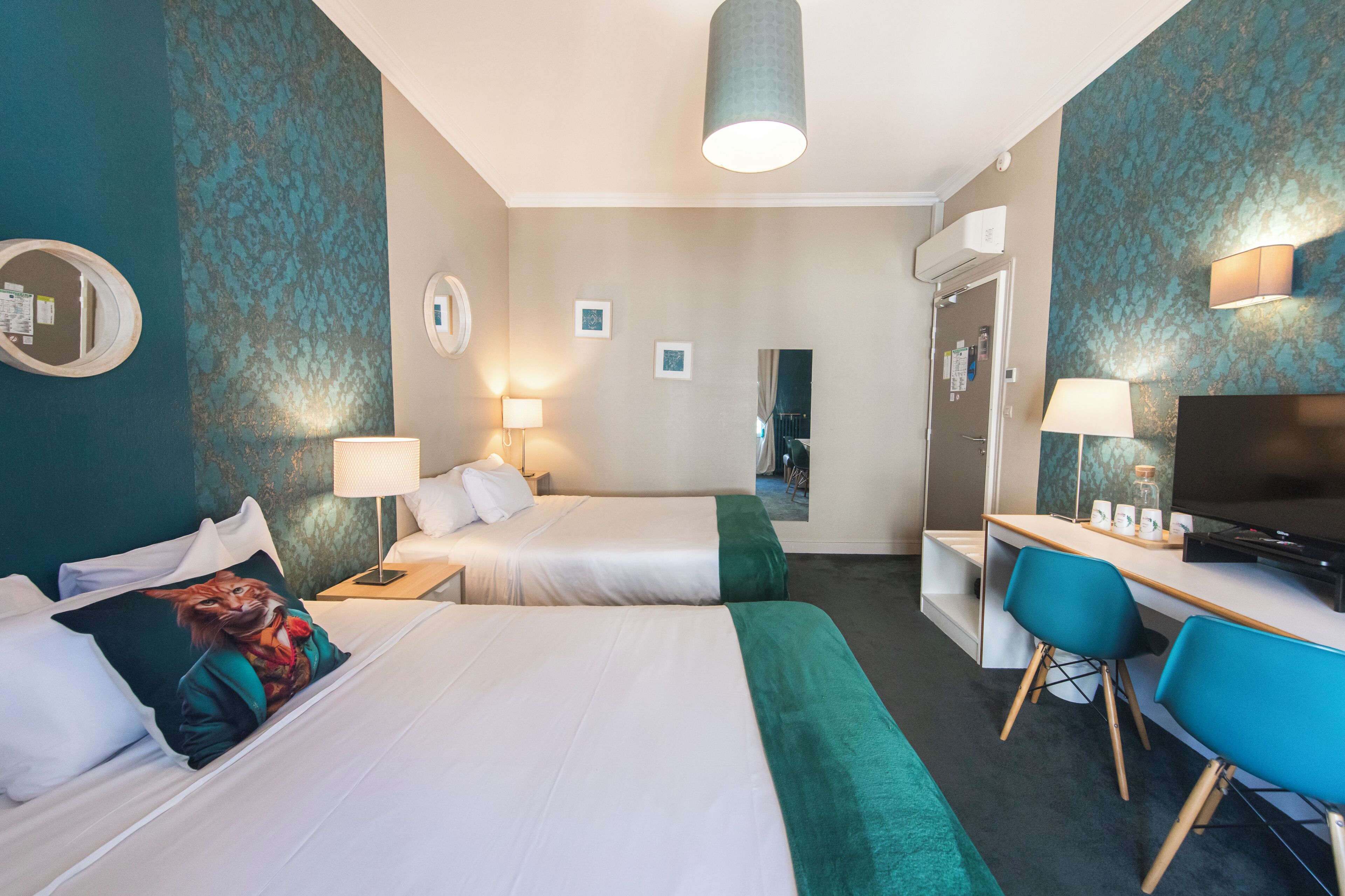 A hotel room with two beds, a desk, a TV, and a mirror.