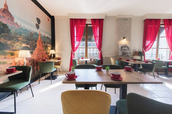 A restaurant with tables and chairs, a Buddha statue, and a mural of a temple.