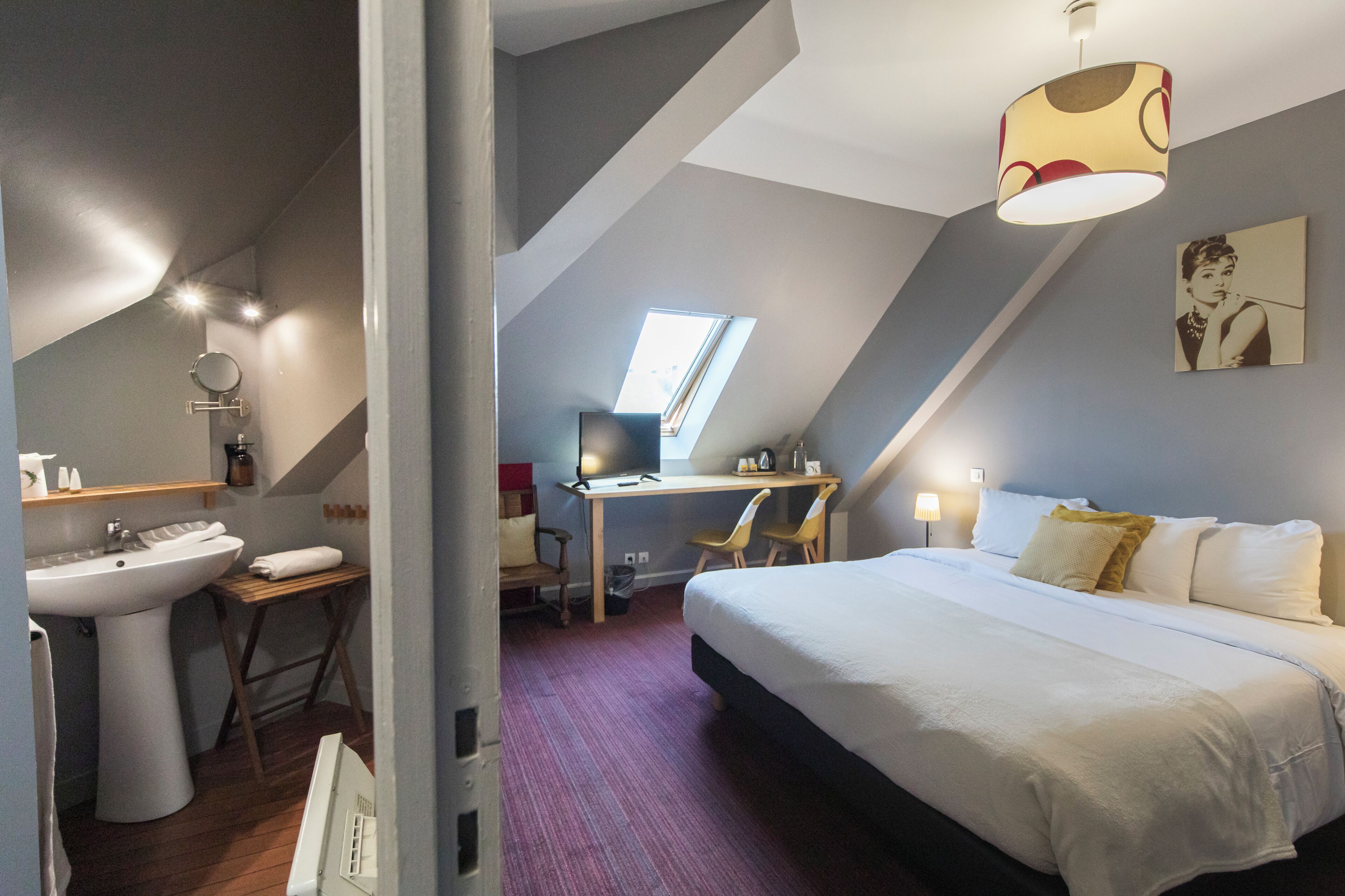 A bedroom with a bed, a desk, a chair, a sink, and a window.