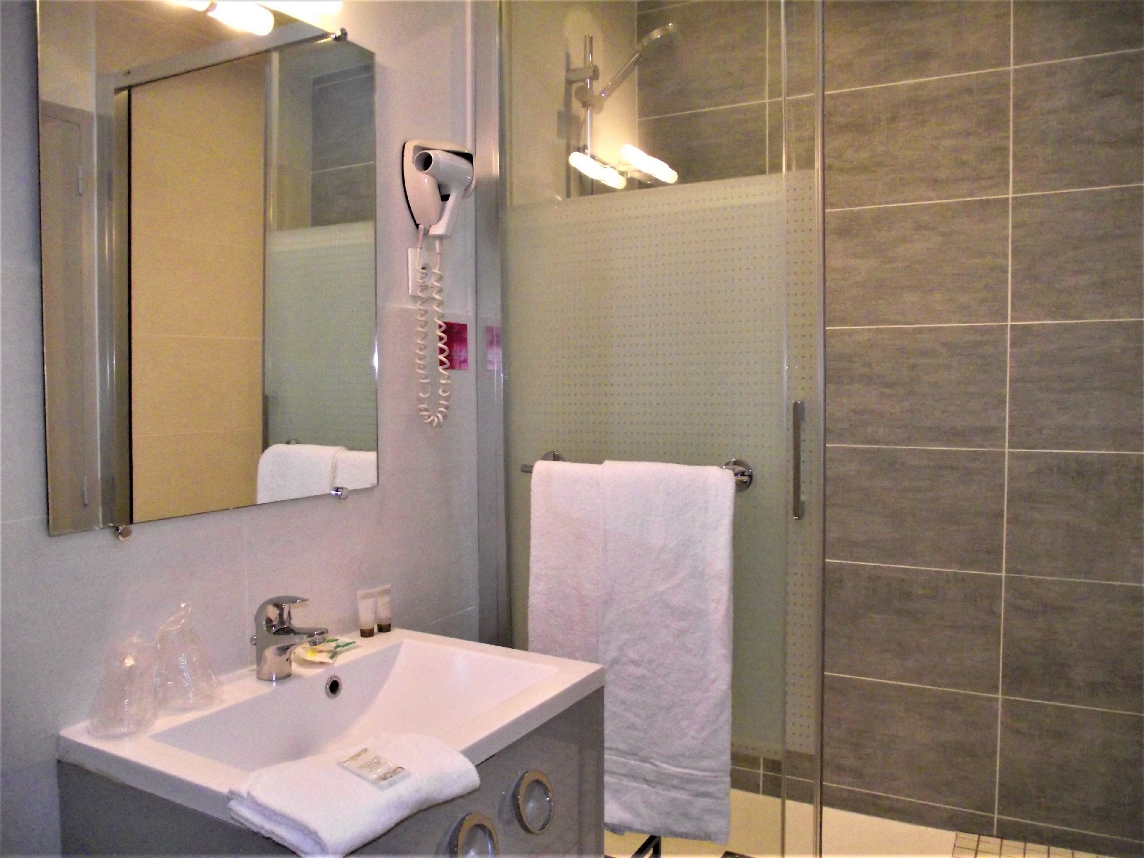 A bathroom with a sink, mirror, hairdryer, and a shower area.