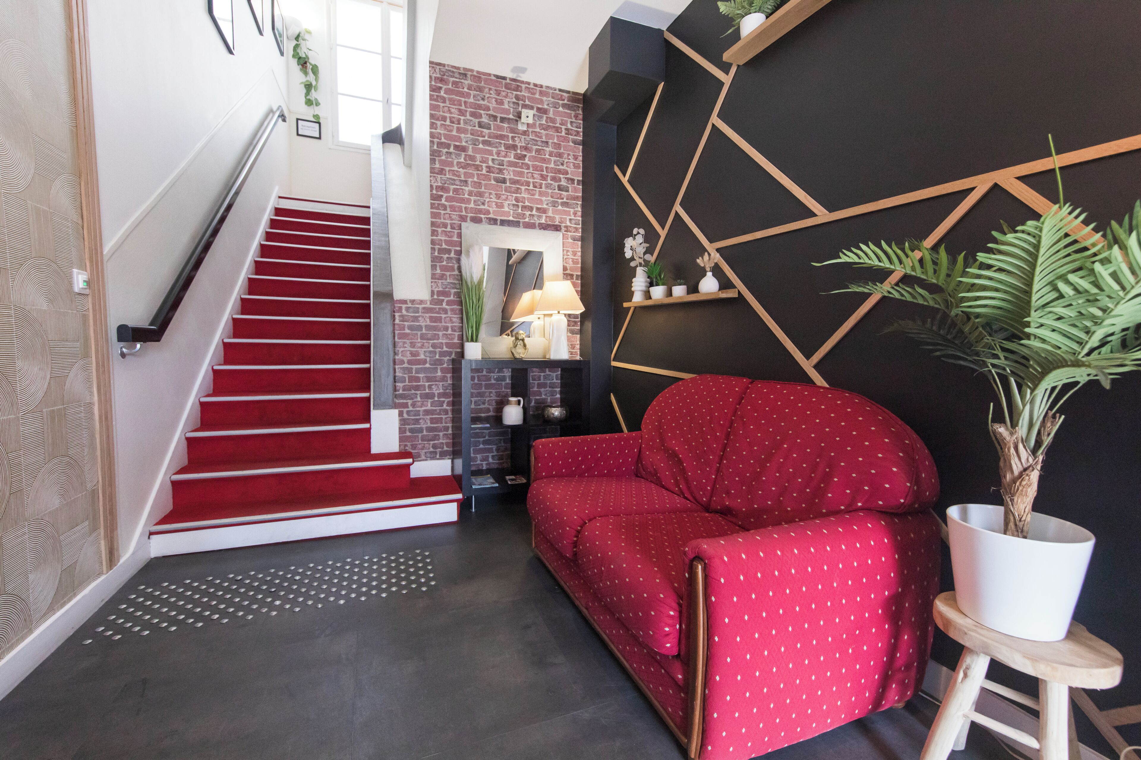 Una escalera con alfombra roja, un sofá rojo, una planta en maceta y un diseño geométrico en la pared.