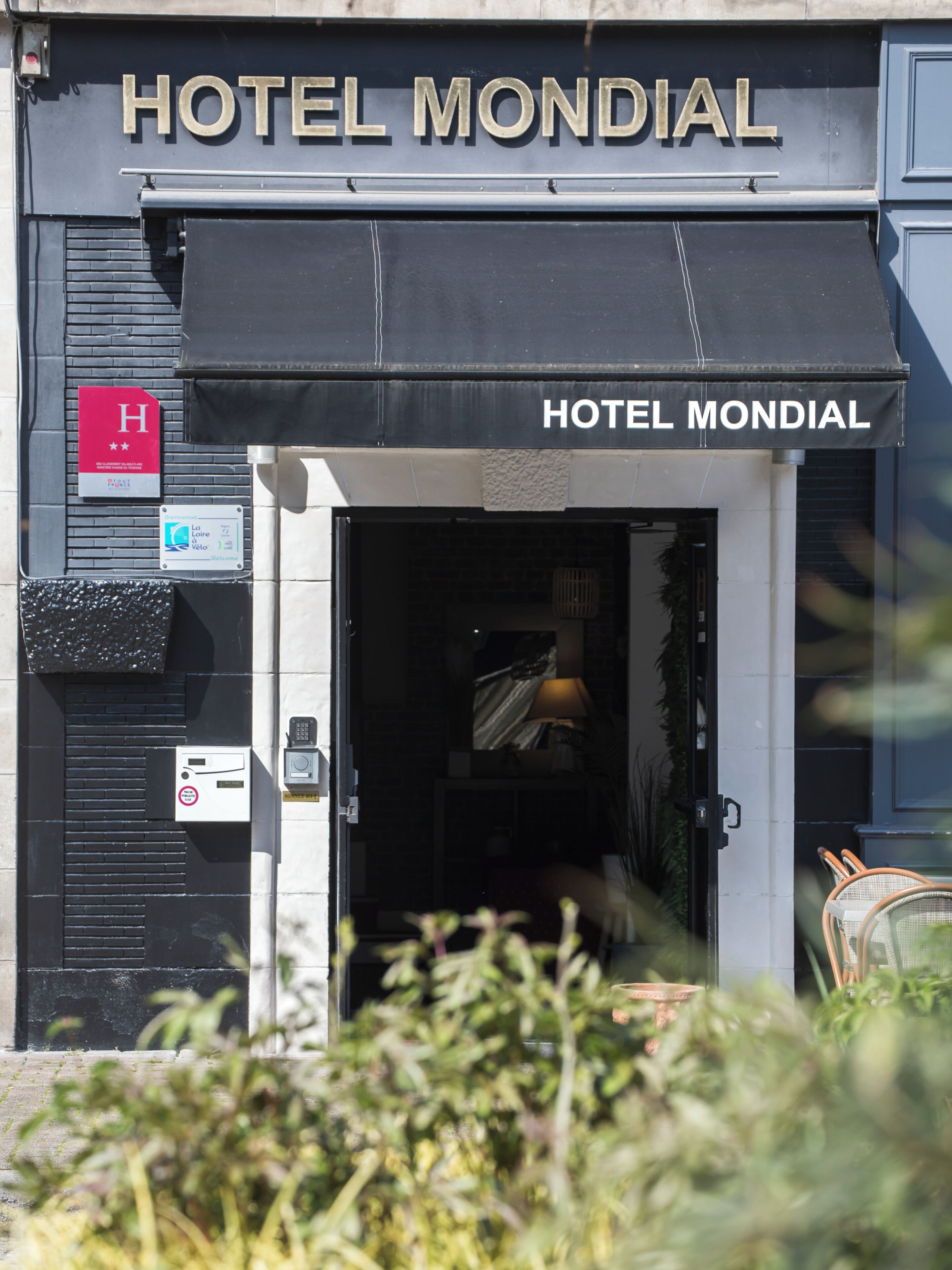 Hotel Mondial set med en sort markise, et rødt skilt med et hvidt 'H' og en glasdør.