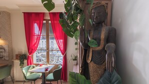 A room with a Buddha statue, a dining table with chairs, a red curtain, and a view through a window. - Hotel Mondial (Tours)