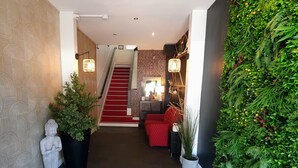 A hotel lobby with a red carpet, a Buddha statue, a world map doormat, and a green wall with plants. - Hotel Mondial (Tours)