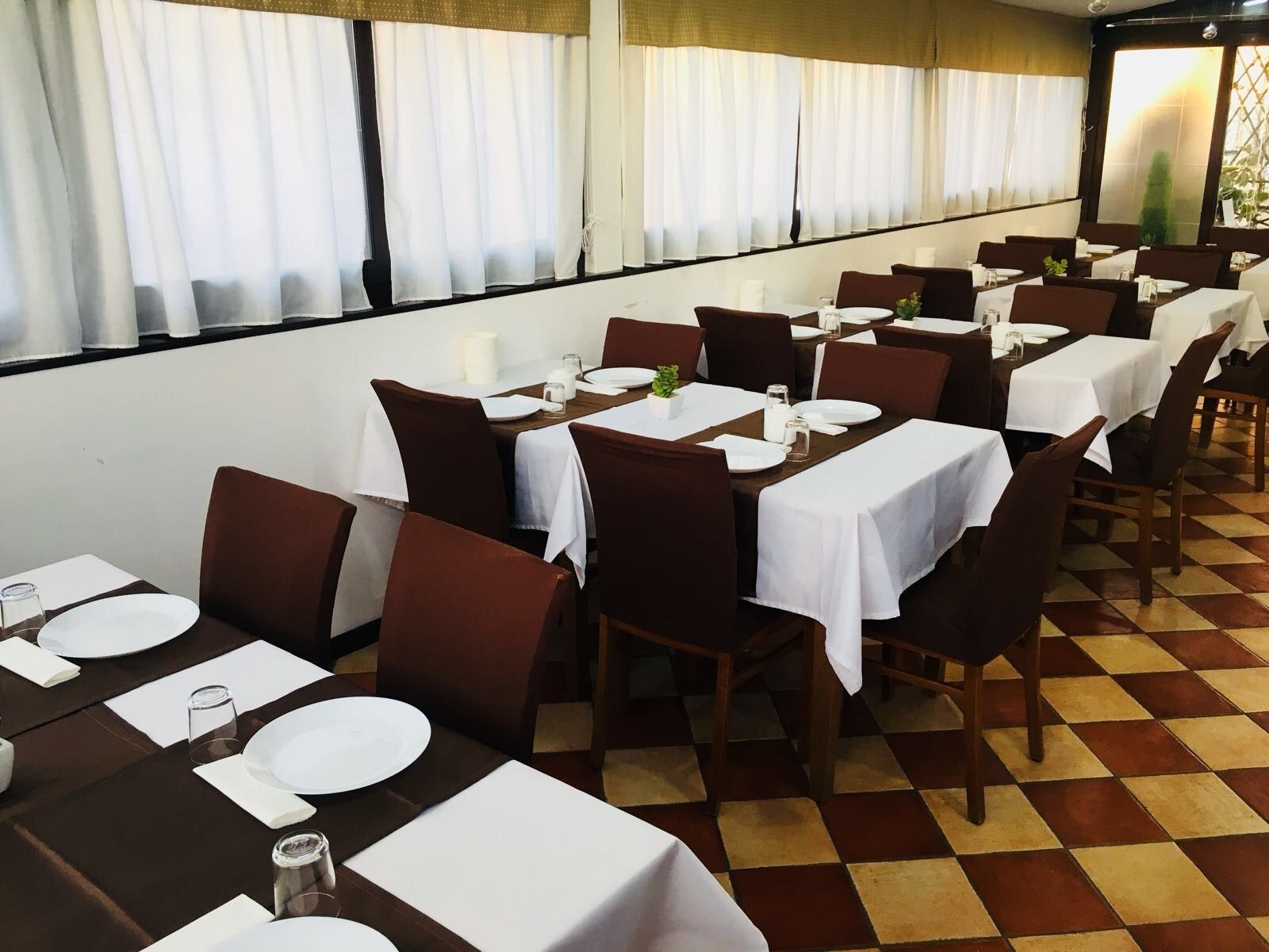 A restaurant with multiple tables set for dining, featuring a checkered floor pattern and white tablecloths.