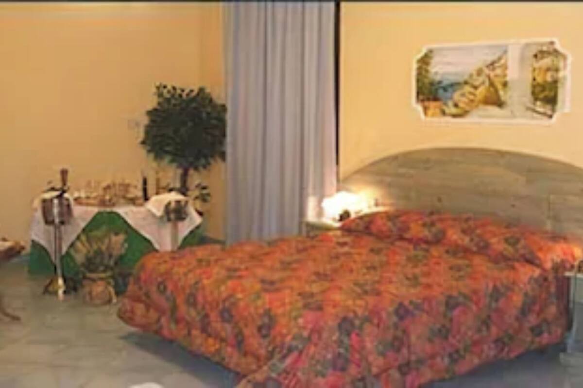 Ein Schlafzimmer mit floralem Bettbezug, einem Nachttisch mit Lampe, einem kleinen Tisch mit Pflanze und einem Gemälde an der Wand.
