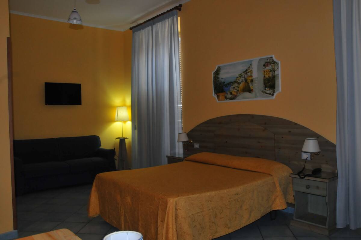 Ein Hotelzimmer mit Bett, Sofa, Fernseher, Lampe und einem Bild an der Wand.