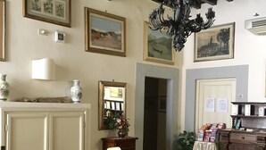 A dining area with a wooden table, chairs, and a chandelier. There are framed pictures on the walls and a cabinet with items on top.