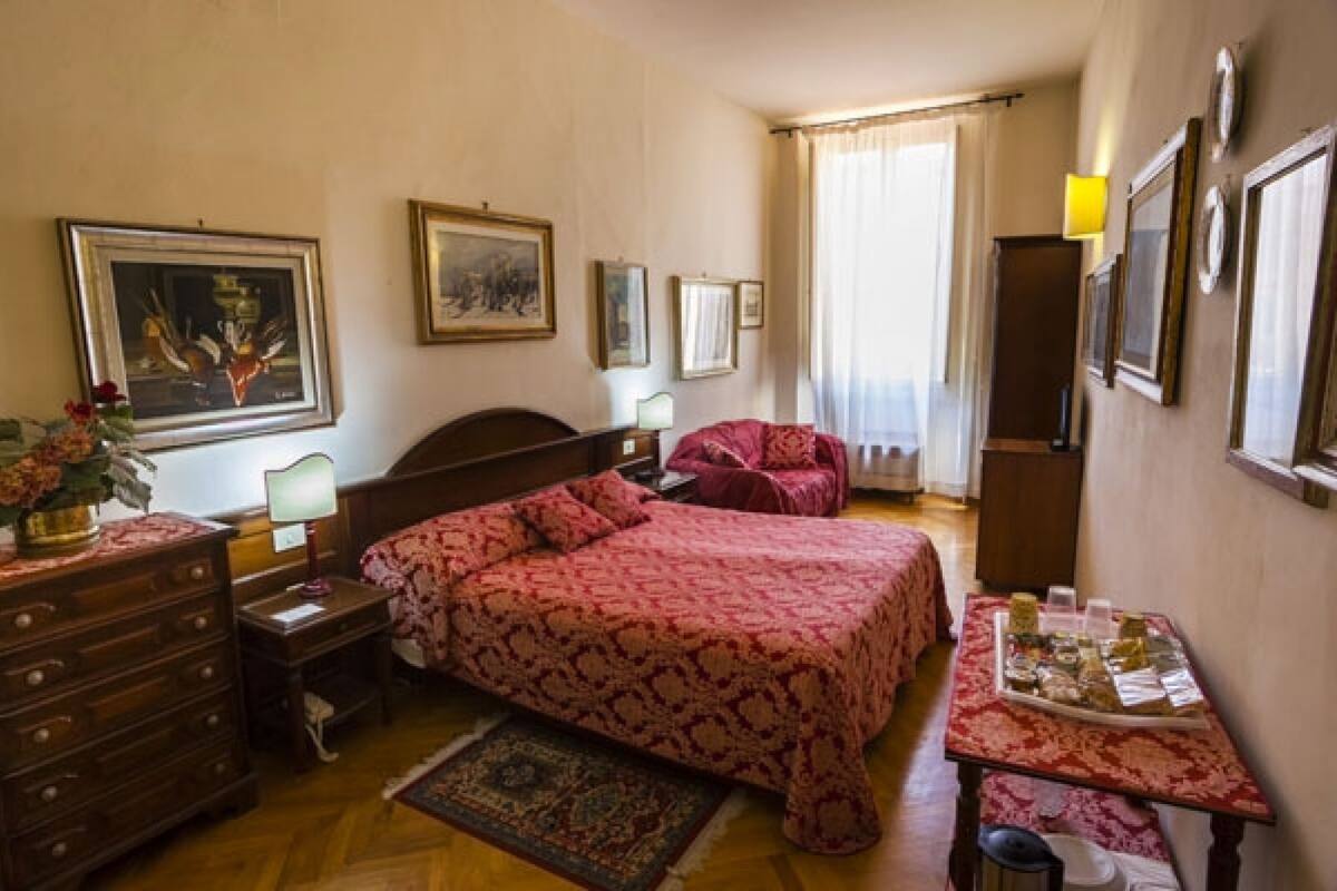A bedroom with a bed, dresser, bedside table, lamp, and a small table with items on it.