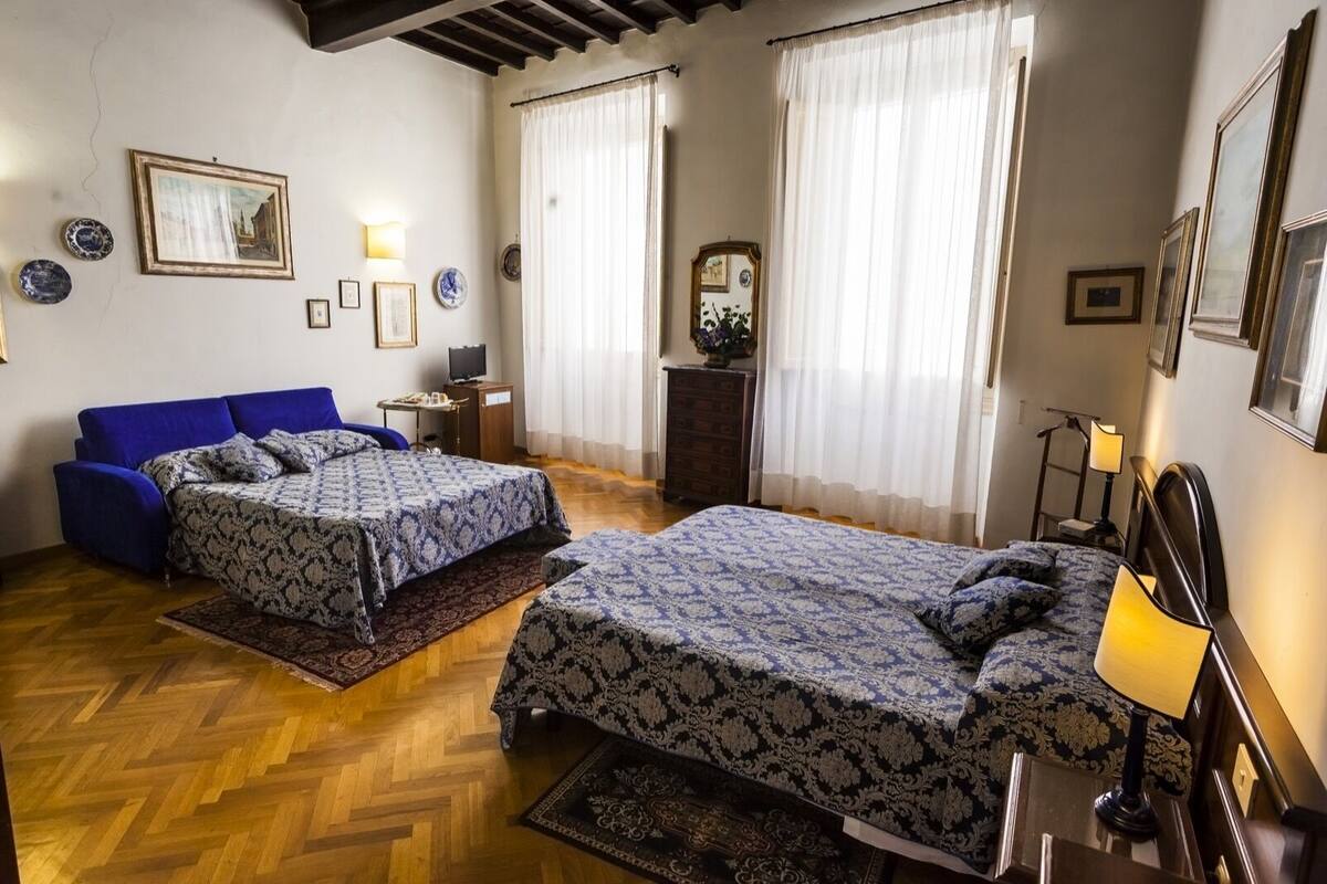 A room with two beds, a blue sofa, a wooden floor, and a mirror on the wall.