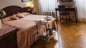 A room with a wooden ceiling, a bed with a pink bedspread, a desk with a chair, and a cart with items.