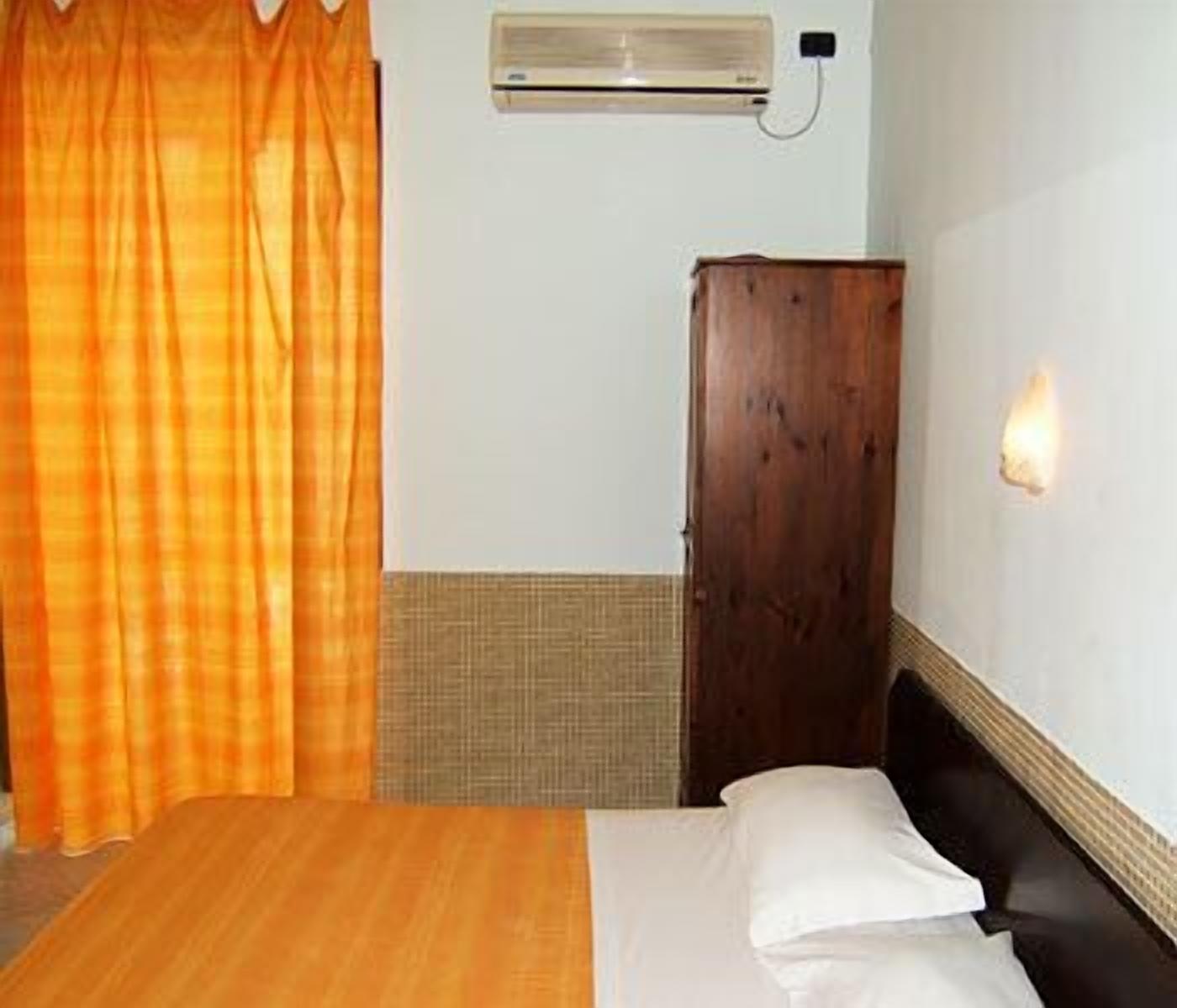 A hotel room with a bed, a wooden wardrobe, a wall-mounted air conditioner, and a curtain.
