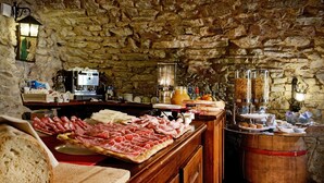 Ein Frühstücksbuffet mit verschiedenen Fleischsorten, Käse und Brot, vor einer Wand aus Stein.