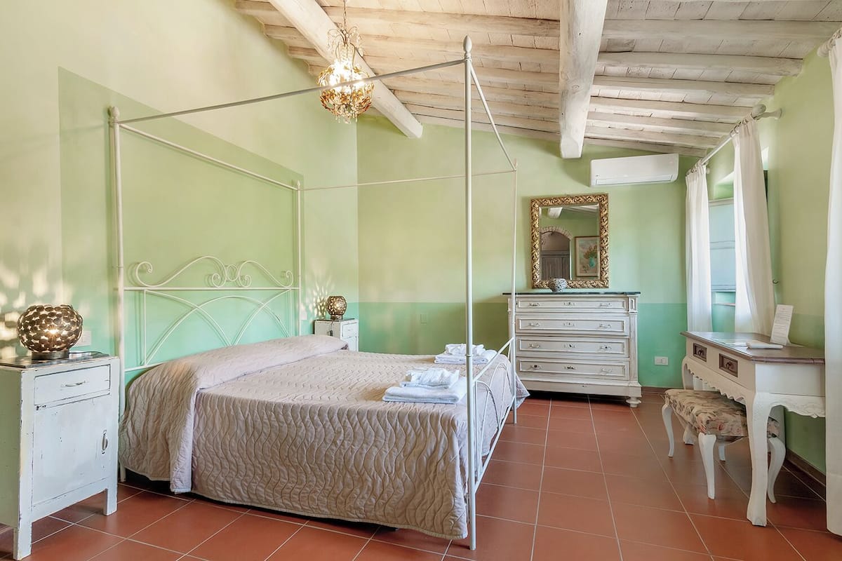A bedroom with a four-poster bed, a dresser, a vanity with a mirror, and a small stool.