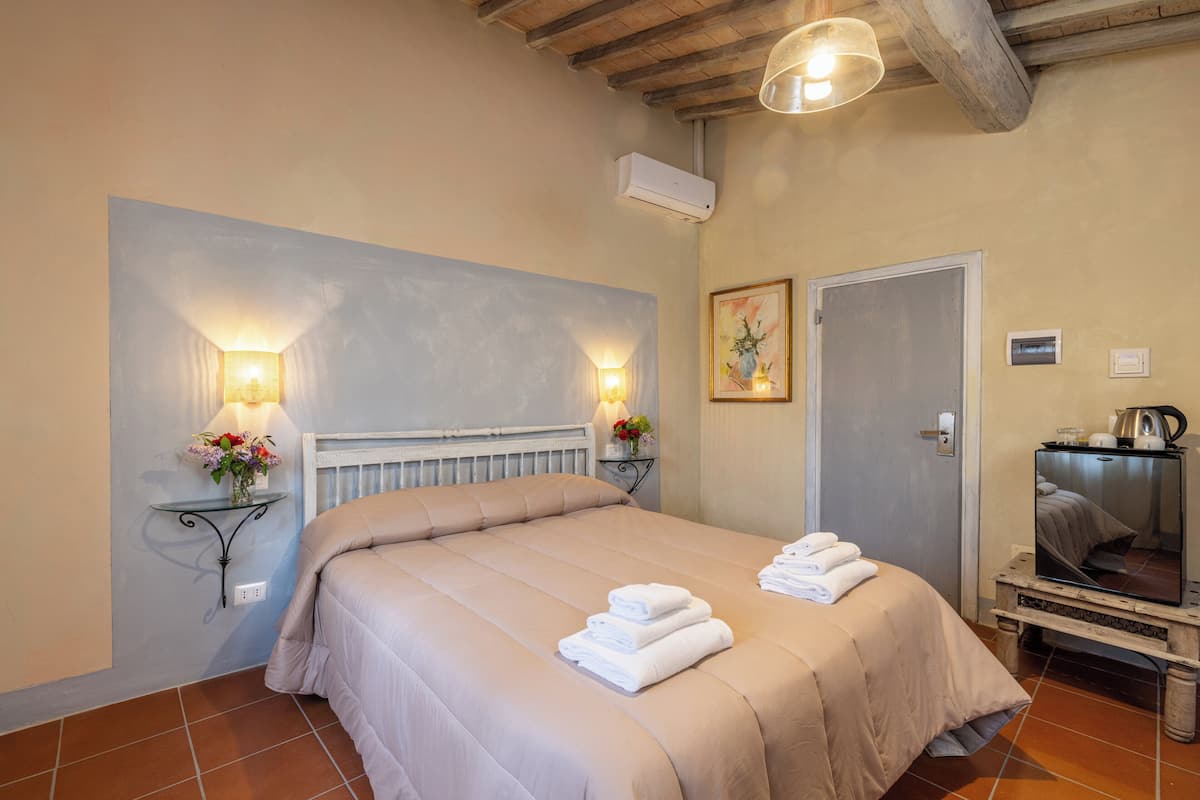 A bedroom with a large bed, two wall-mounted lamps, a radiator, a door, and a television on a wooden stand.