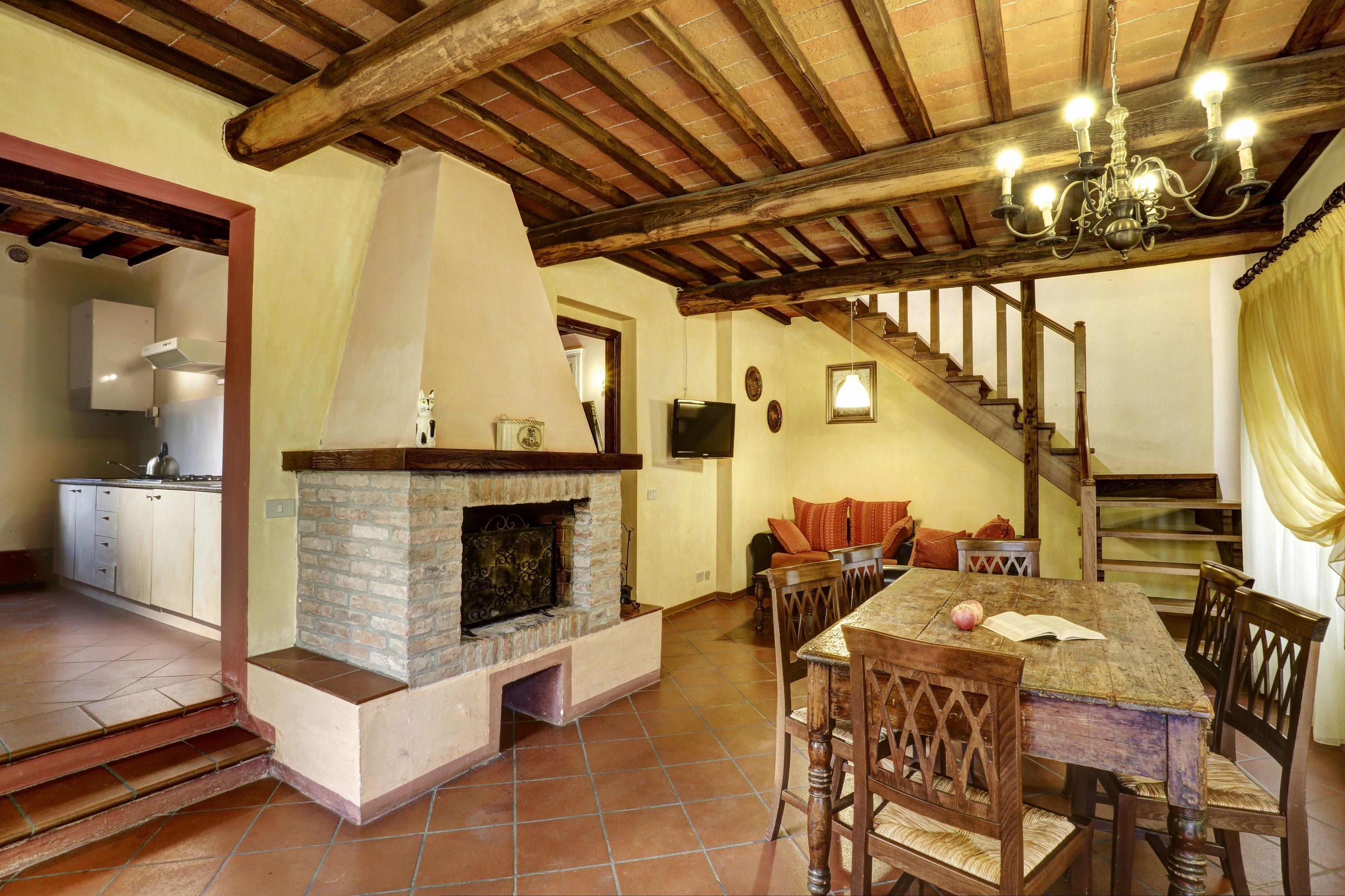 A rustic interior with a stone fireplace, wooden dining table, and a staircase leading to an upper level.