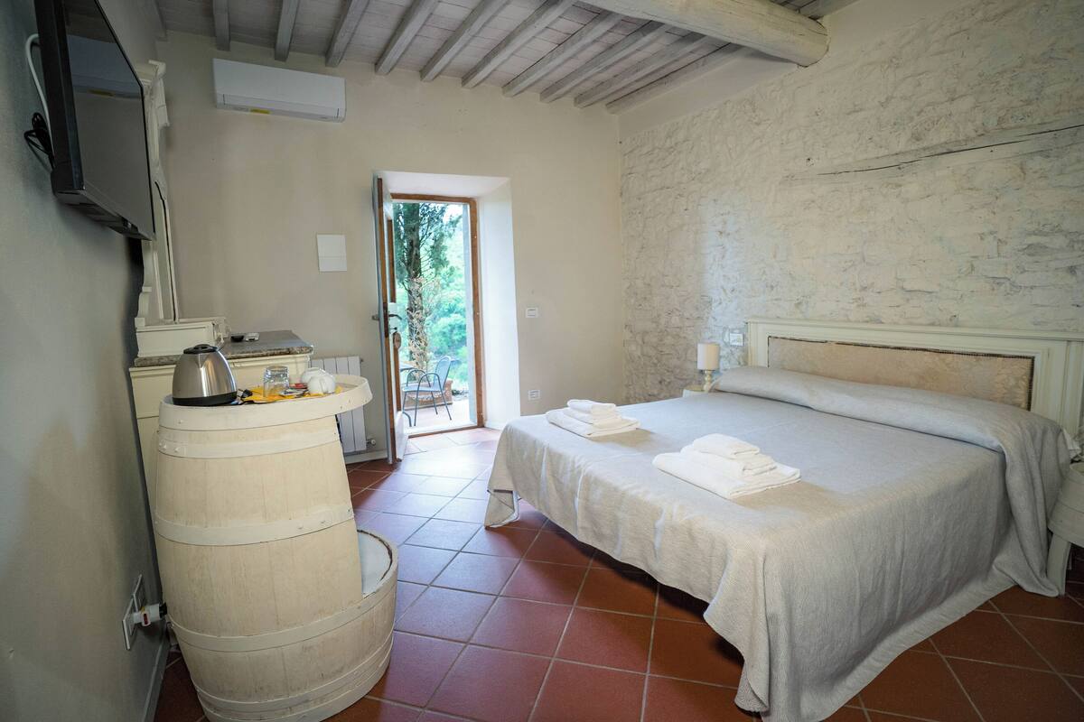 A bedroom with a bed, a wooden barrel, a television, and a window with a view of greenery.