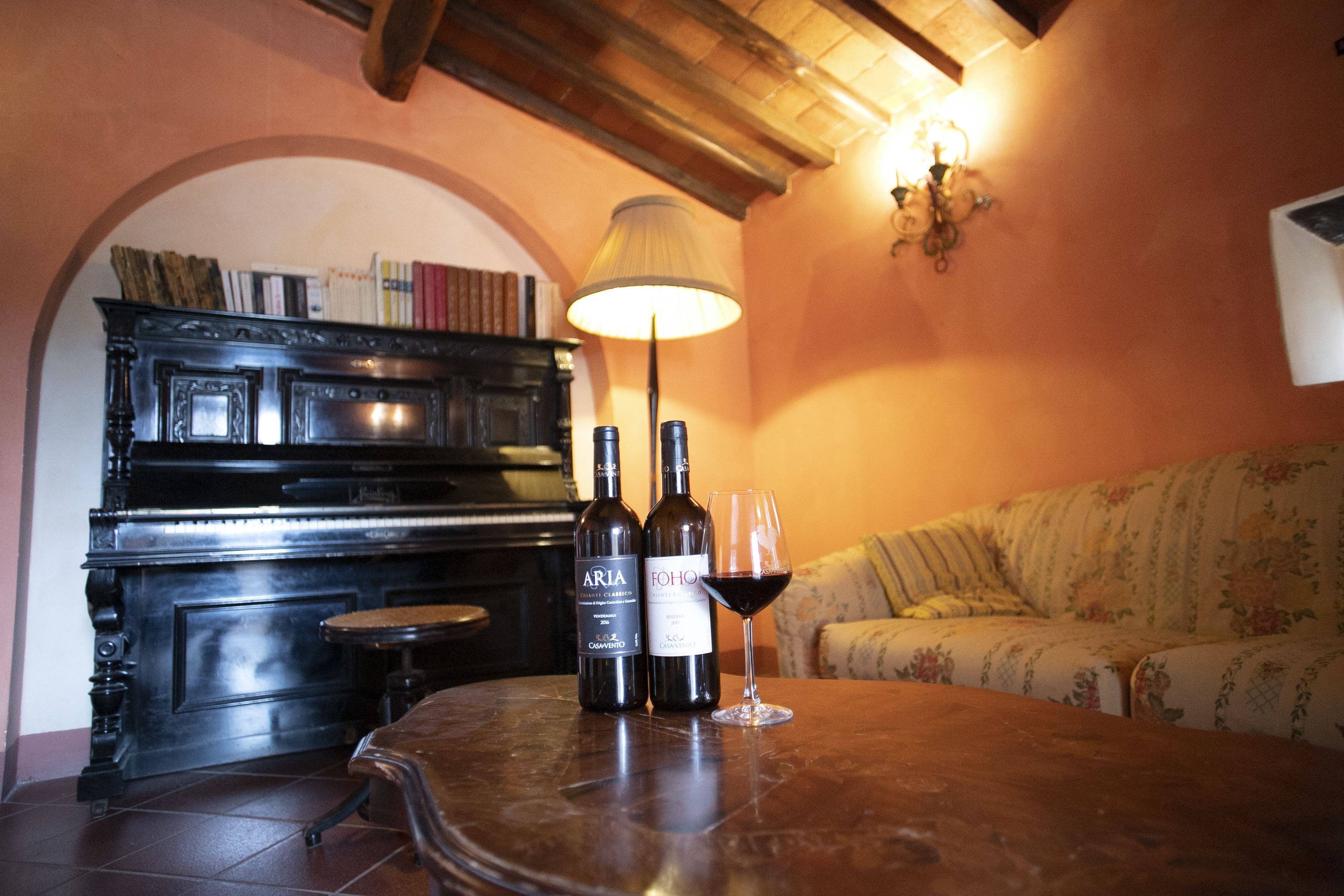 Ein Zimmer mit einem Klavier, zwei Weinflaschen und einem Glas Rotwein auf einem Tisch.
