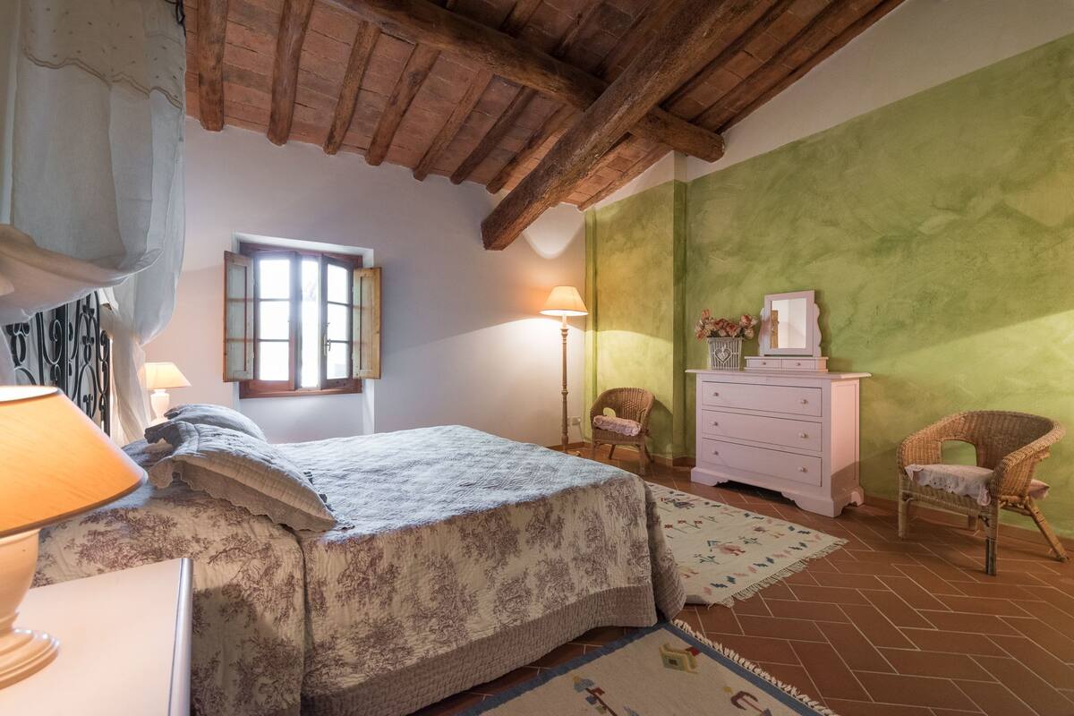 A bedroom with a bed, two chairs, a dresser, and a window.