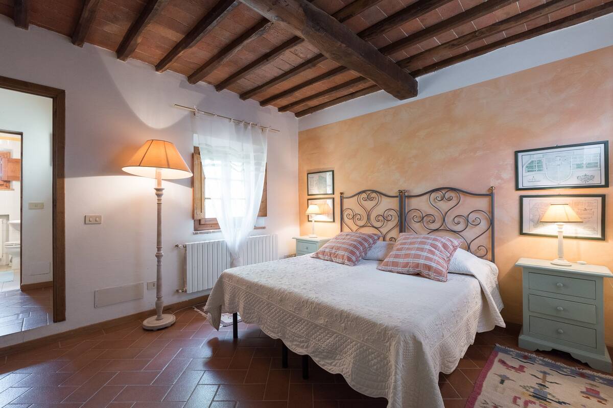 A bedroom with a bed, two bedside tables, a floor lamp, and a window with curtains.