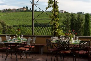 An outdoor dining area with tables set for two, chairs, and a view of vineyards in the background. - Podere Torricella (Montespertoli)