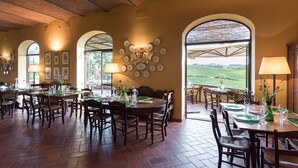 A dining area with multiple tables and chairs, a brick floor, and a view of the countryside through large windows. - Podere Torricella (Montespertoli)