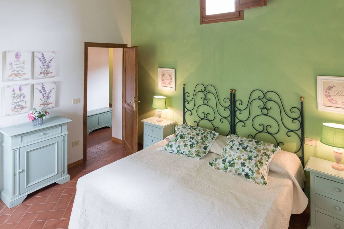 A bedroom with a wooden ceiling, green walls, a bed with floral pillows, and a small window.
