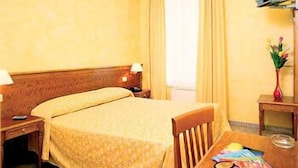 A hotel room with a double bed, a wooden nightstand with a lamp, a small table with a book and a vase of flowers. - Hotel Kriss (Rome)