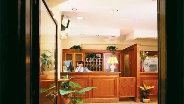 A reception area with a wooden counter, potted plants, and a tiled floor. - Hotel Kriss (Rome)