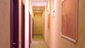A hotel hallway with multiple doors, a tiled floor, and a wall-mounted emergency exit sign. - Hotel Kriss (Rome)