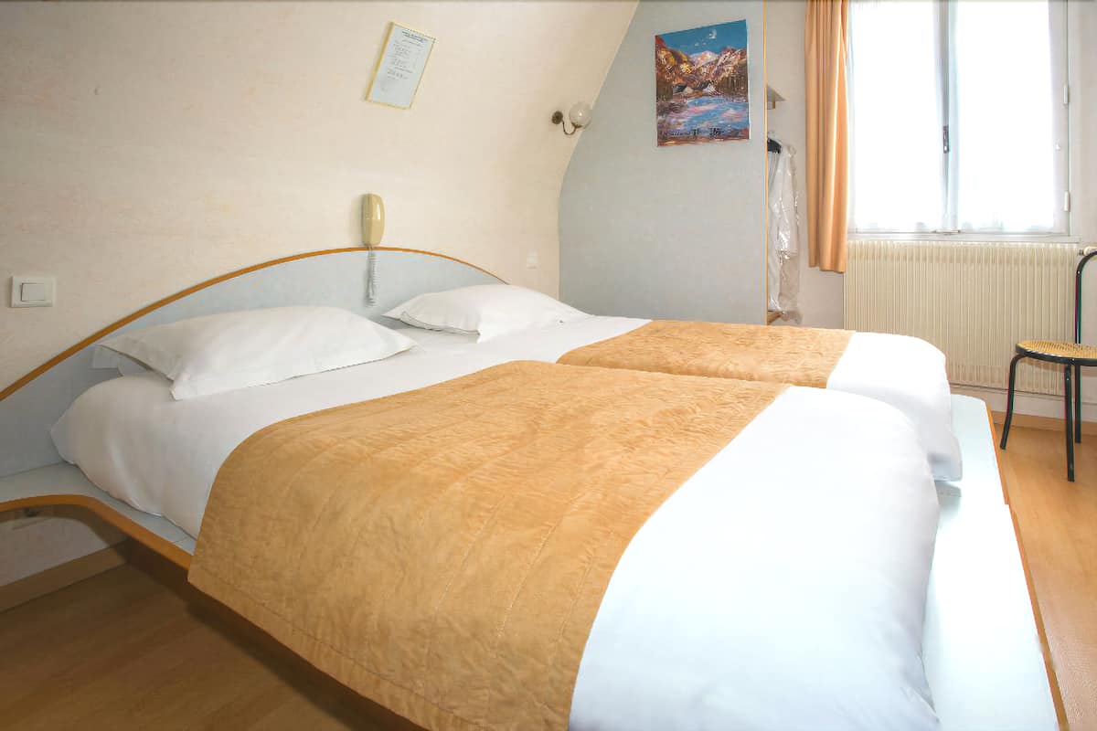 A double bed with white and brown bedding, a bedside telephone, and a window with curtains.